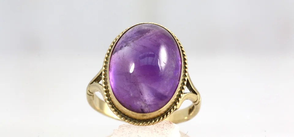 A purple cabochon gemstone in an ornate gold ring